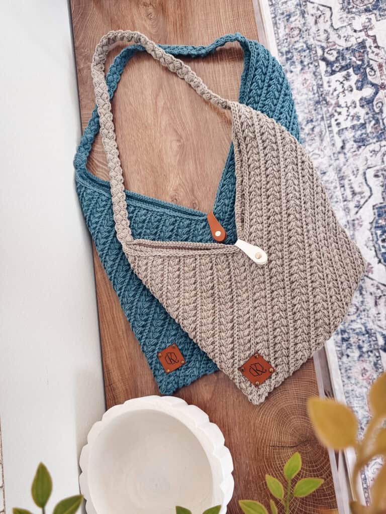 Two knitted bags, one teal and one beige, with leather tags and handles, are placed on a wooden surface beside a white bowl and green plant—perfect inspo for your next Wheat Stitch Crochet Rectangle Bag Pattern project.