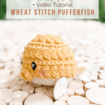 A crocheted yellow pufferfish with white fins sits on a wood slice surface. Text above reads: "Free Crochet Pattern + Video Tutorial Wheat Stitch Pufferfish.