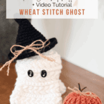 A crocheted white ghost with black button eyes and a black witch hat sits next to a small crocheted orange pumpkin on a wooden surface.