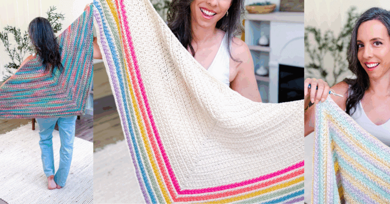 A woman displays a large crocheted shawl with colorful stripes, holding it open and smiling in a bright room with plants and a fireplace in the background.