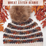 A multicolored Wheat Stitch Crochet Beanie with a large faux fur pompom is displayed on a white background with autumn leaves, promoting a free crochet pattern and video tutorial.