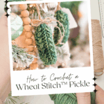 A hand holds a photo of two crocheted green pickles hanging on a Christmas tree, with text promoting the free Wheat Stitch Crochet Pickle Ornament Pattern and video tutorial.