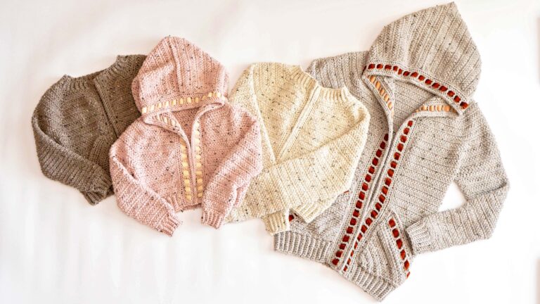 Four Cascade Adult Crochet Cardigans, knitted in grey, pink, cream, and light grey with red trim, are laid out side by side on a white background.