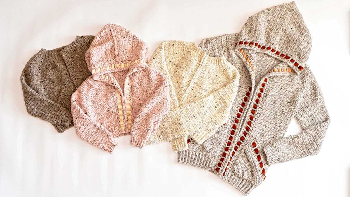 Four Cascade Adult Crochet Cardigans, knitted in grey, pink, cream, and light grey with red trim, are laid out side by side on a white background.