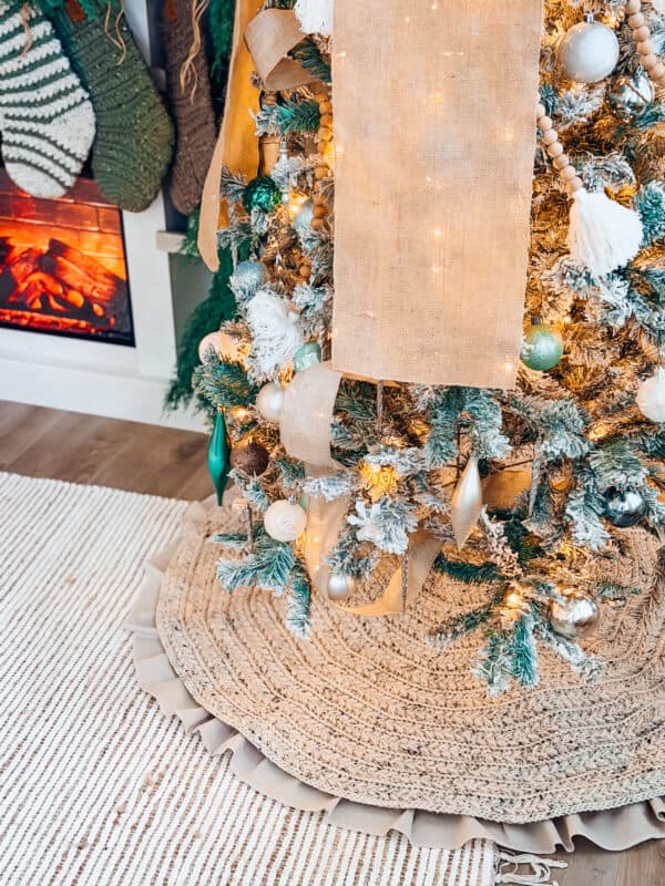 A decorated Christmas tree with ribbon, ornaments, and lights stands on a Wheat Stitch Crochet Tree Skirt Pattern near a fireplace and hanging stockings.