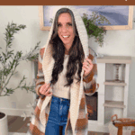 Woman wearing a cream-colored crocheted hooded scarf, standing indoors in a living room, with text promoting a free wheat stitch scarf crochet pattern and video tutorial.