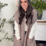 Woman wearing a knitted wheat stitch pocket shawl in a cozy indoor setting; text reads "How to Crochet a Wheat Stitch Pocket Shawl, Free Pattern + Video Tutorial.