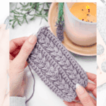 A person holds a crocheted swatch in progress with a crochet hook, next to a lit candle and some greenery on a table—perfect for practicing different crochet skill levels.