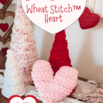 Three crocheted heart-shaped cones in white, pink, and red yarn are displayed on a wooden surface with heart decorations and flowers nearby. Text offers a crochet heart pattern and tutorial.