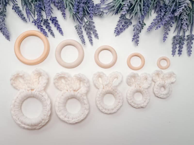 Seven wooden rings of varying sizes are arranged in a row below sprigs of lavender; four of the rings are wrapped in white yarn to resemble bunny ears.