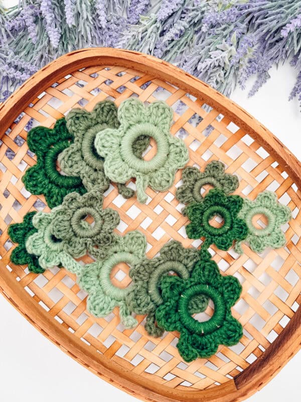 A woven basket holds several green crochet flowers in varying shades, with lavender sprigs in the background.