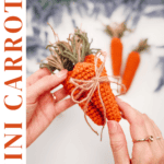 Hands holding a crocheted mini carrot tied with twine, with two more crocheted carrots and purple flowers blurred in the background. Text reads: How to Crochet Mini Carrots—perfect for pairing with any Crochet Bunny Head Pattern.