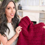 Woman holding a large, red Petal Loop Stitch Blanket and smiling at the camera; text above reads “You can crochet this” with eye emojis.
