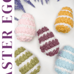 Five crocheted Easter eggs in pastel colors are arranged on a white surface with sprigs of purple flowers. Text promotes a free wheat stitch crochet pattern and video tutorial.