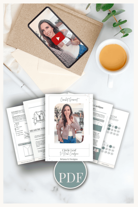 Flat lay of a PDF knitting pattern, Circle Leaf V-Neck Crochet Cardigan pattern instruction sheets, a cup of tea, an envelope, a phone showing a woman, and a plant on a white surface.