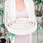 Person in a crochet cardigan holds a coiled, cream-colored crochet storage basket with greenery, featuring text: "Modern Crochet: Storage Project You'll Use." Discover inspiration for your next crochet nesting trays pattern.