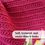 A close-up of a textured, pink crochet Petal Loop Stitch Blanket with the text "Soft, textured, and easier than it looks" overlaid at the bottom. Some blurred green and yellow shapes in the foreground.