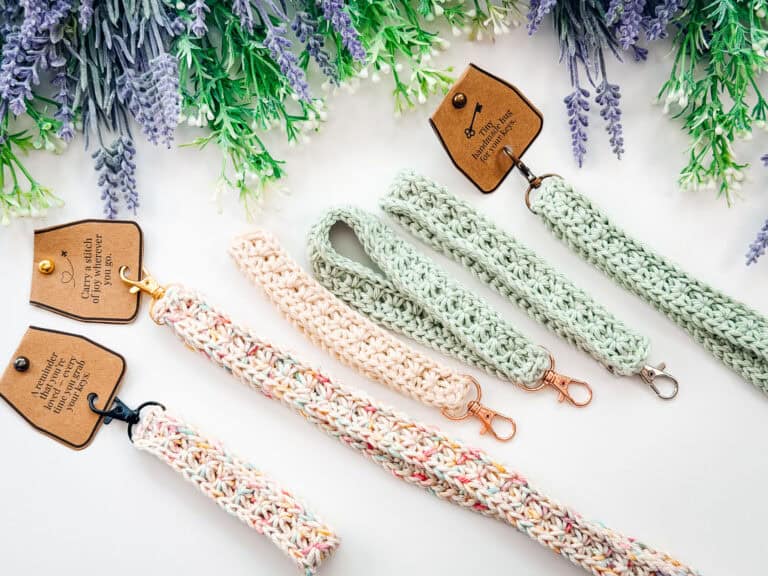 Five crocheted keychain wristlets in pastel colors with metal clasps are displayed on a white surface, set below lavender and green foliage—a charming match for any crochet nesting trays pattern lover.