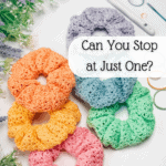 Five crocheted hair scrunchies in various colors are displayed on a white surface with scissors, a crochet hook, artificial flowers, and a crochet nesting trays pattern. Text reads: "Can You Stop at Just One?.
