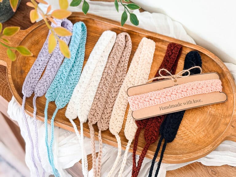 A wooden tray displays crocheted headbands in various colors, with two pink headbands wrapped in paper labeled "Handmade with love.