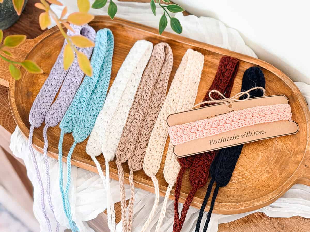A wooden tray displays crocheted headbands in various colors, with two pink headbands wrapped in paper labeled "Handmade with love.