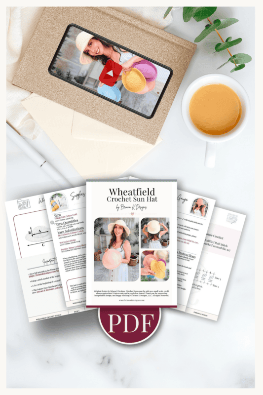 Flat lay of a crochet sun hat PDF pattern, instructional pages, an envelope with a photo of a woman holding hats, a cup of coffee, and a sprig of greenery on a white surface.