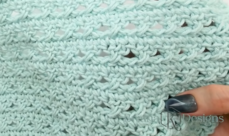 Close-up of a hand holding light blue knitted fabric with a textured, openwork stitch pattern.