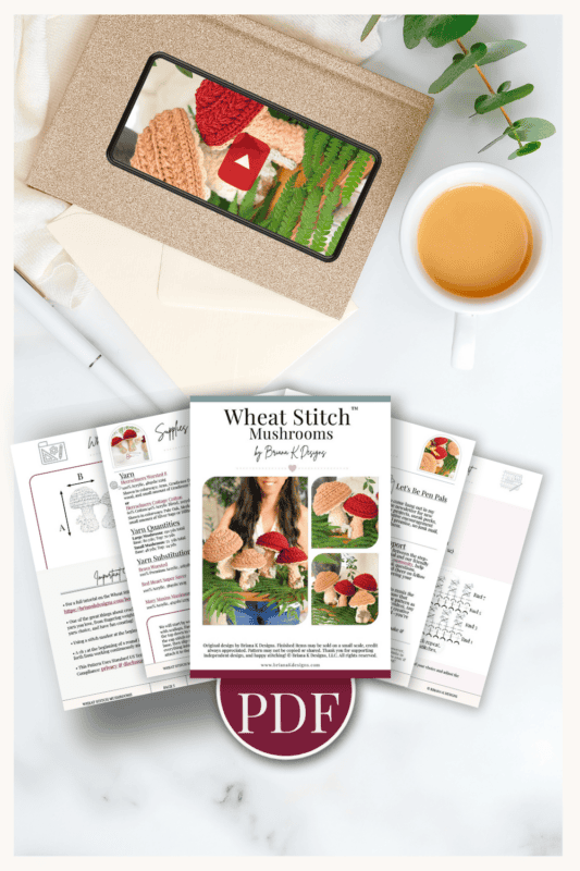 A PDF crochet pattern for mushrooms is displayed on printed pages, with a coffee cup, envelope, and plant arranged around it on a light surface.