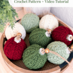 A wooden bowl holds red, green, and white crochet Christmas ornaments topped with wooden beads, beside a green plant.