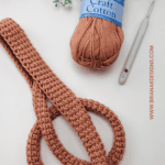 A crocheted Tunisian simple stitch strap is shown alongside a ball of Village Yarn Craft Cotton and a crochet hook. Text reads "Tunisian Simple Stitch Strap Free Video Tutorial.