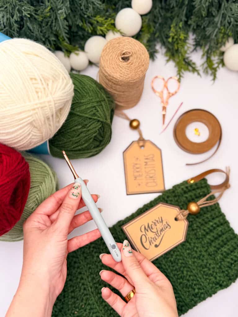 Briana's hands holding a crochet hook with gold snips and tags nearby