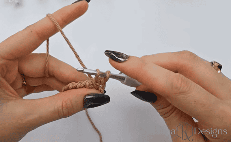 Close-up of hands holding a crochet hook and yarn, demonstrating the process of creating crochet stitches against a plain background.