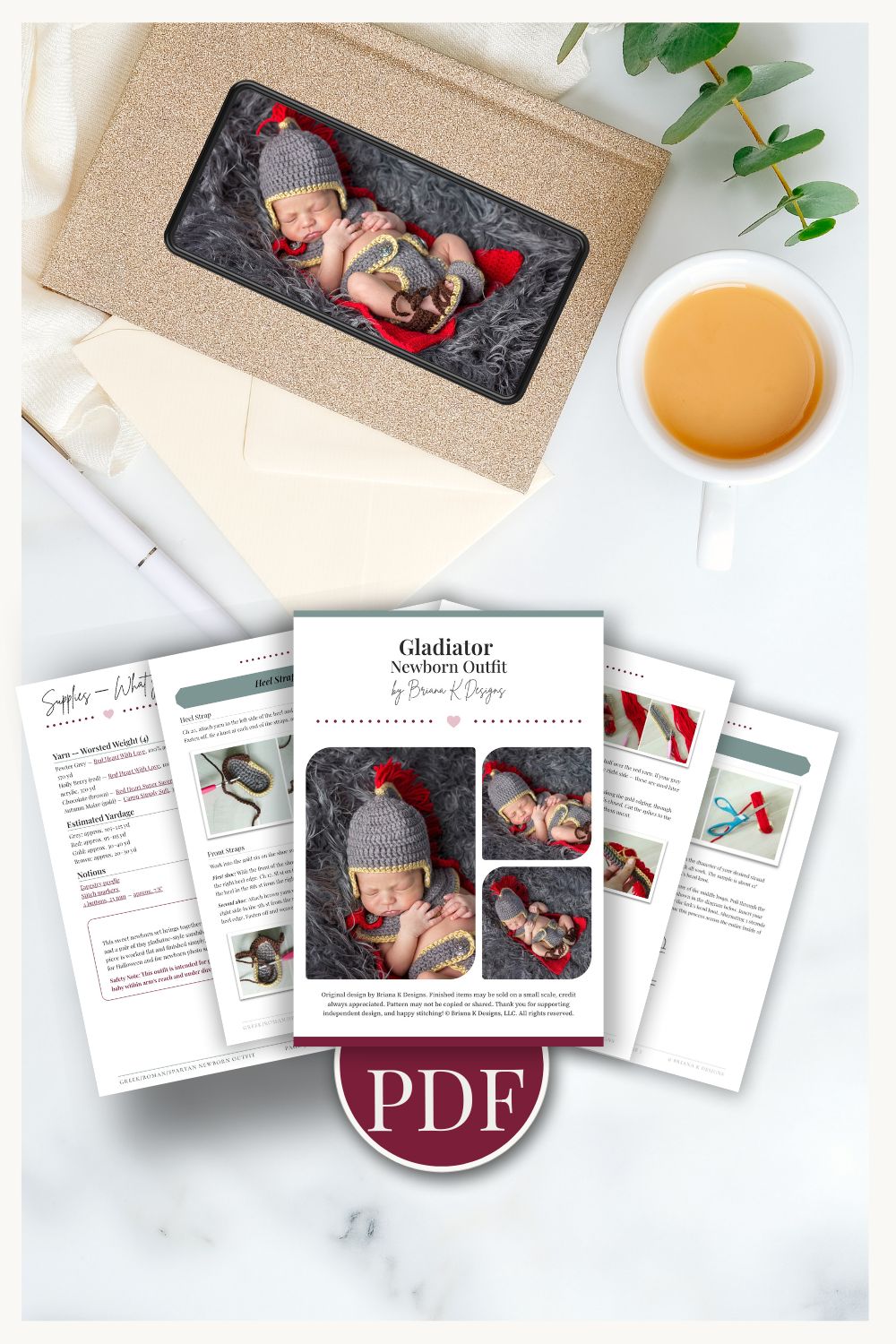 Flat lay of a PDF tutorial for an odyssey gladiator crochet baby outfit, with printed pages, a cup of tea, a leafy branch, and a boxed baby photo in costume arranged on a white surface.