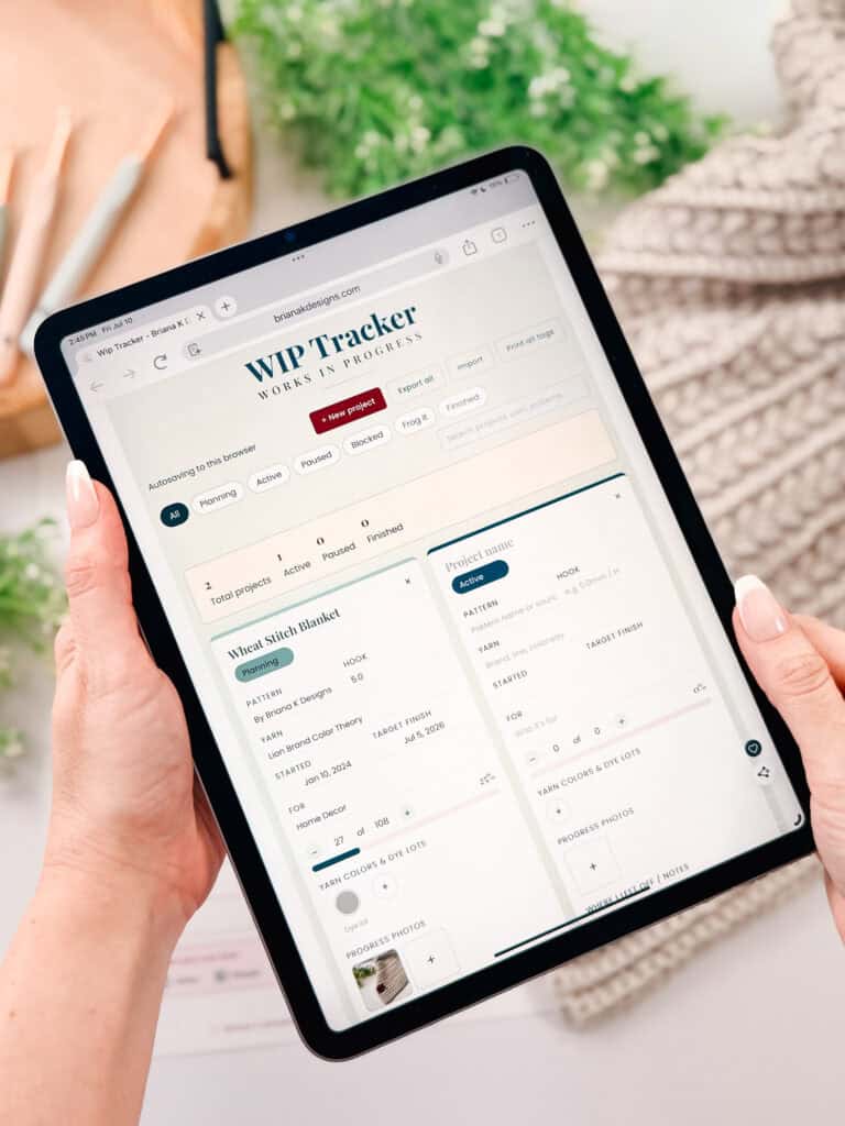 Person holding a tablet displaying a crochet WIP tracker webpage for managing knitting or crochet projects, with sections for project name, pattern, yarn, and project status.