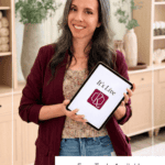Woman in a burgundy blazer holds a tablet displaying “It’s Live K” under a banner that reads “The Briana K App is here! Free Tools Available.” She stands in a modern, neutral-toned room.