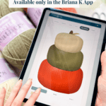 A person holding a tablet displaying a digital illustration of three stacked pumpkins in different colors, with yarn skeins in the background.