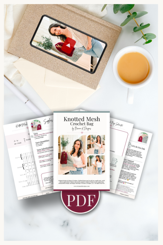 Flat lay of a crochet pattern PDF for a knotted mesh bag, shown with printed pages, a photo album, cup of coffee, pen, and green leaves on a white surface.