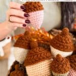 A hand holds a crocheted acorn above a basket filled with more crocheted acorns. Text overlay reads: “Wheat Stitch Acorns Free Crochet Pattern + Video.”.