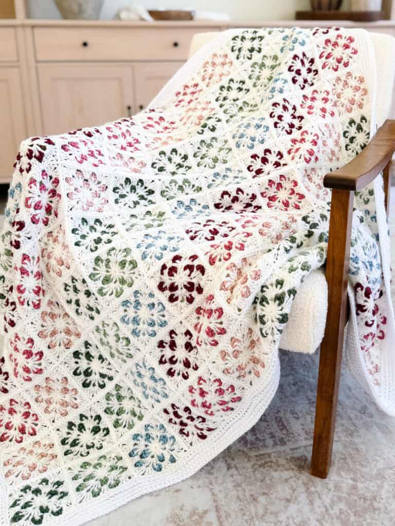 Crocheted blanket with colorful floral square patterns draped over a wooden armchair in a cozy room.