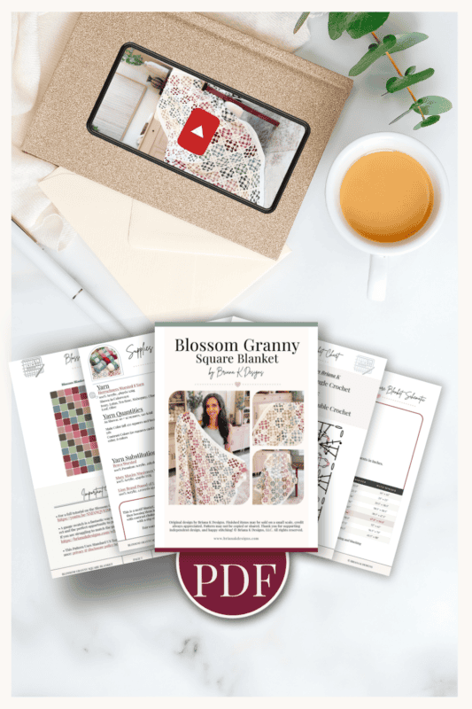 A Blossom Granny Square Blanket crochet PDF pattern with instruction pages, an envelope, a cup of tea, and a sprig of greenery displayed on a white surface.