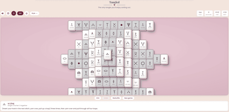 A digital Mahjong Solitaire game is displayed on a pink background, showing various tiles stacked in a complex, tangled arrangement. Reminiscent of a crochet solitaire game, the playful design adds cozy charm to the classic puzzle. Game controls and instructions are visible.