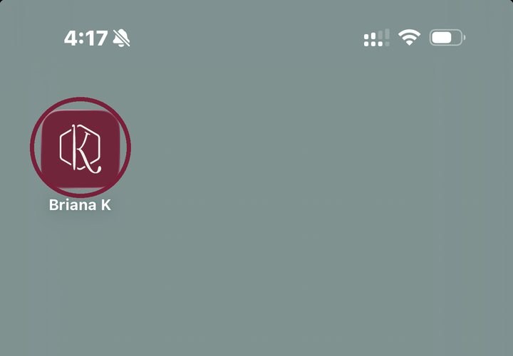 Smartphone screen showing a single app icon labeled “Briana K” with a maroon circle and stylized letters, on a plain gray background. The status bar displays time, network, and battery icons. The app’s unique design hints at creative features, making it perfect for fans of the trending crochet game genre.