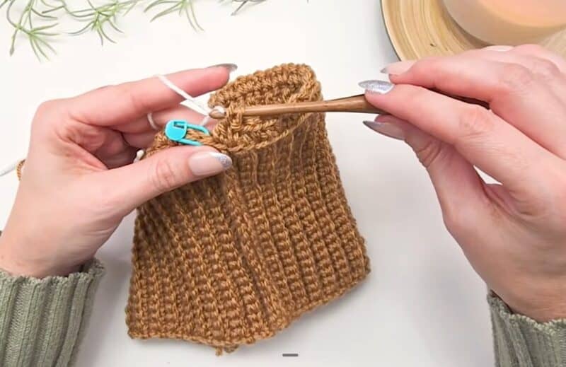 A camel ribbed crochet beanie brim with single crochet worked evenly around the top edge, joined in the round with a blue stitch marker at the join