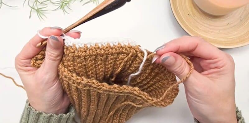 A cream round of the houndstooth stitch worked across a camel crochet beanie, with the unused camel yarn dropped and waiting at the seam inside the work