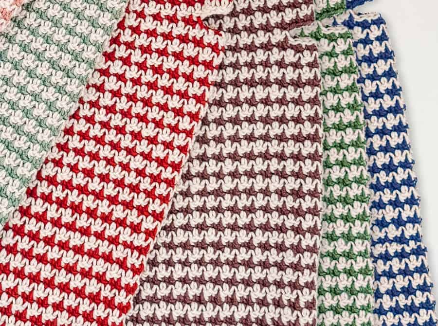 Close-up of the crochet houndstooth stitch on four dog sweaters in red, brown, green and cobalt blue, each paired with cream, showing the staggered broken checks