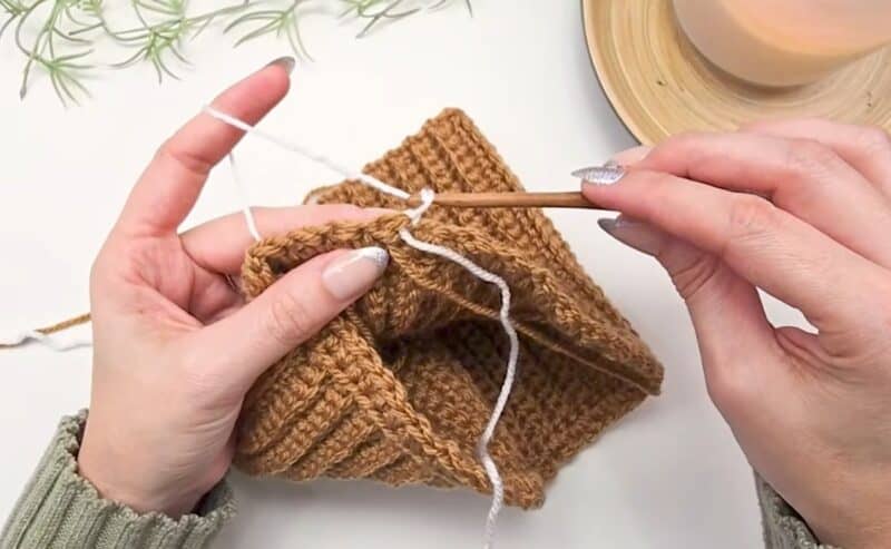 Hands pulling cream yarn through at the join of a camel crochet round to change colors for the next houndstooth round