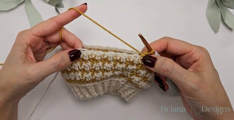 Hands holding a cream and mustard houndstooth crochet panel at the end of a row, with the mustard yarn on the hook to start the next row