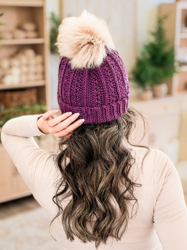 Back view of the Petal Loop Crochet Beanie in purple with a faux fur pom-pom, showing the seam and the ribbed fold-up brim