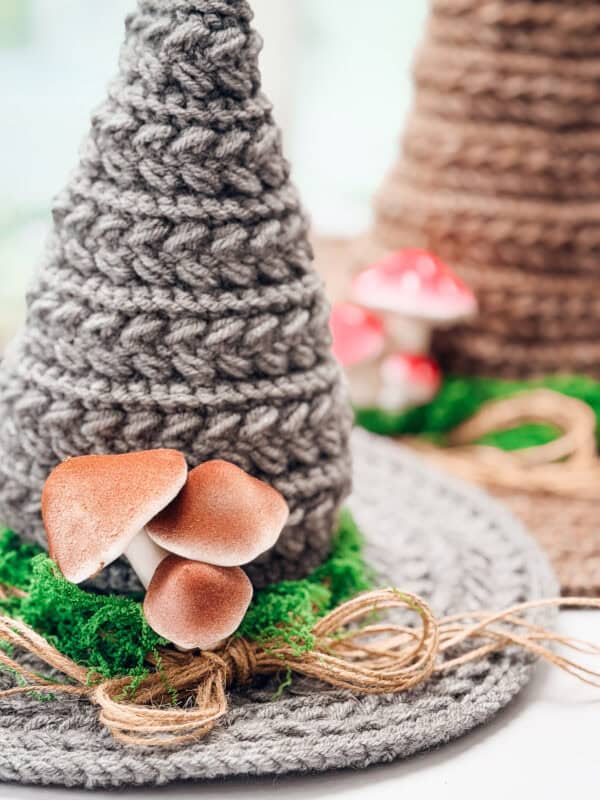 Close up of a gray Wheat Stitch crochet witch hat with mushrooms, moss and a jute twine band