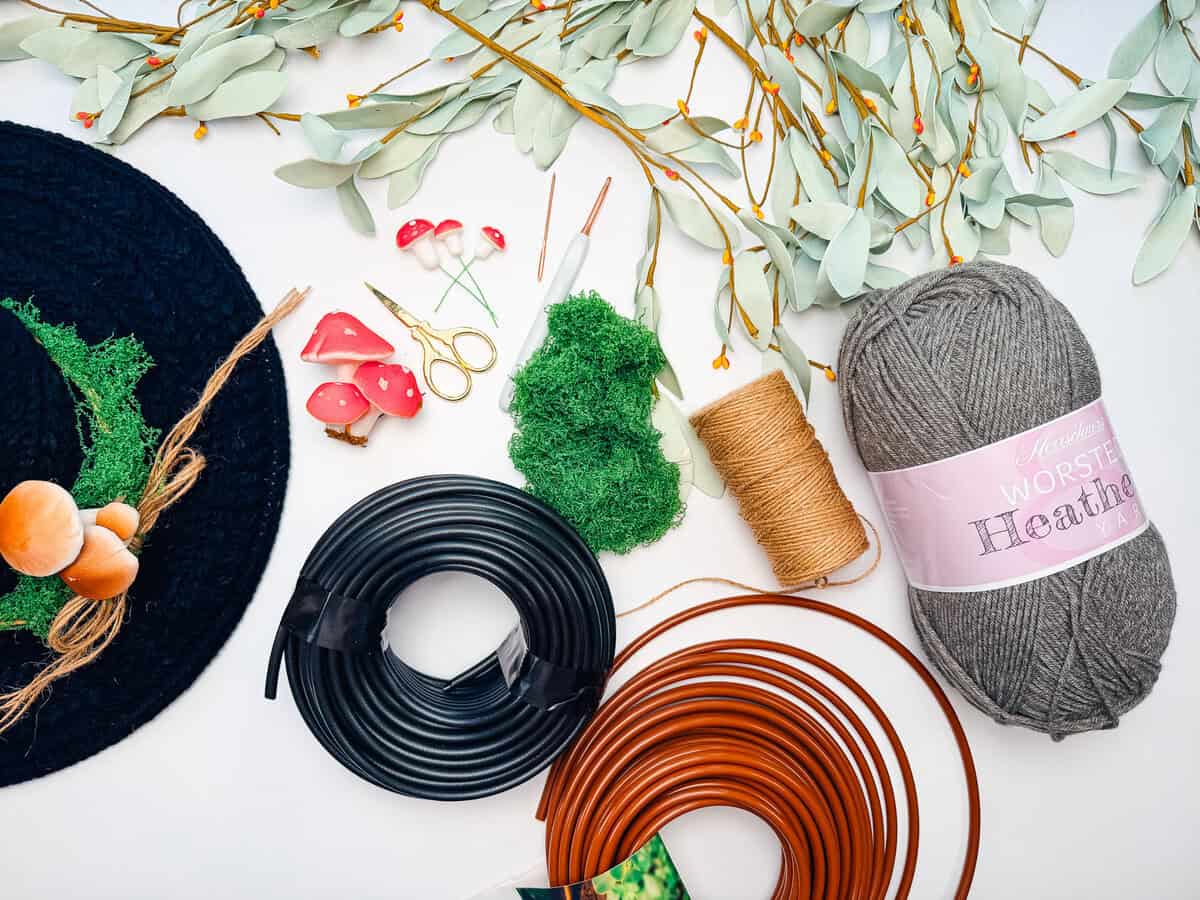 Supplies for a crochet witch hat pattern: gray yarn, memory wire, drip tubing, jute twine, moss, mushrooms and scissors